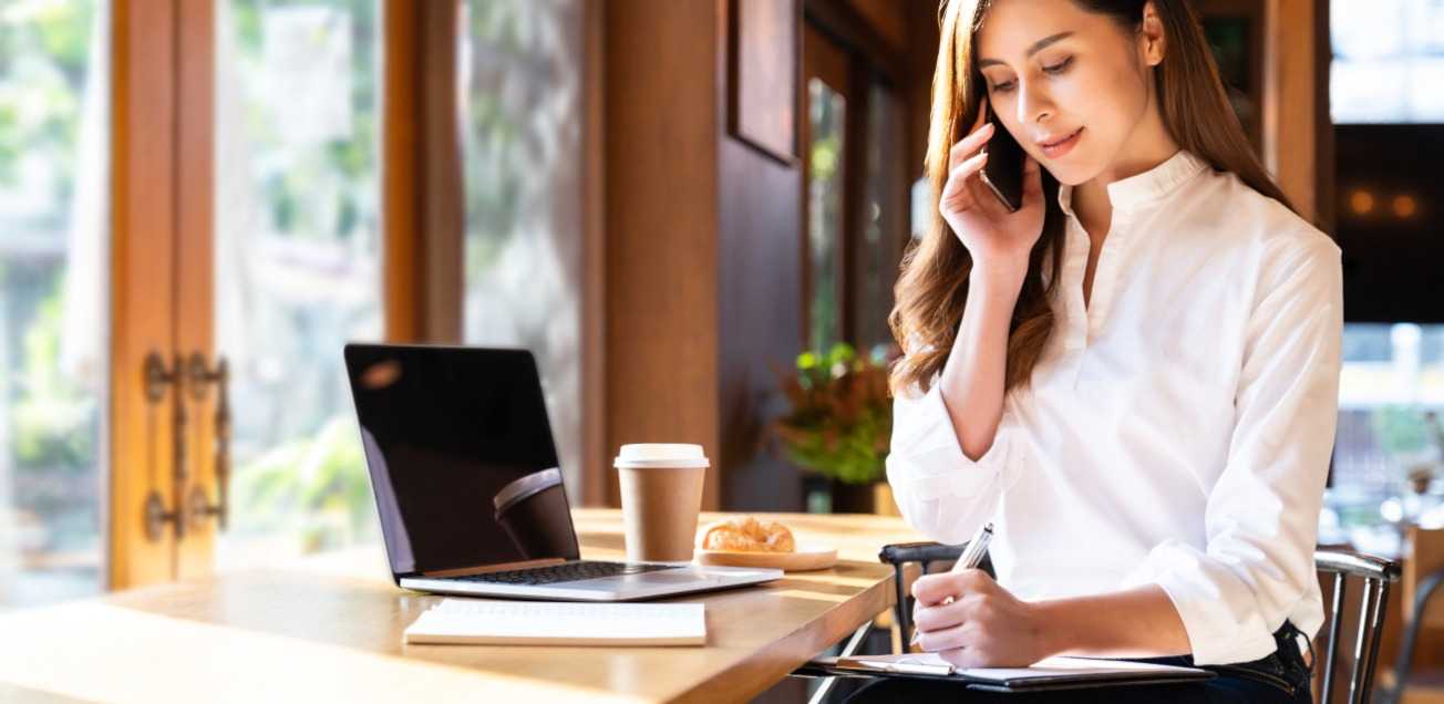 Business woman taking notes while on a call